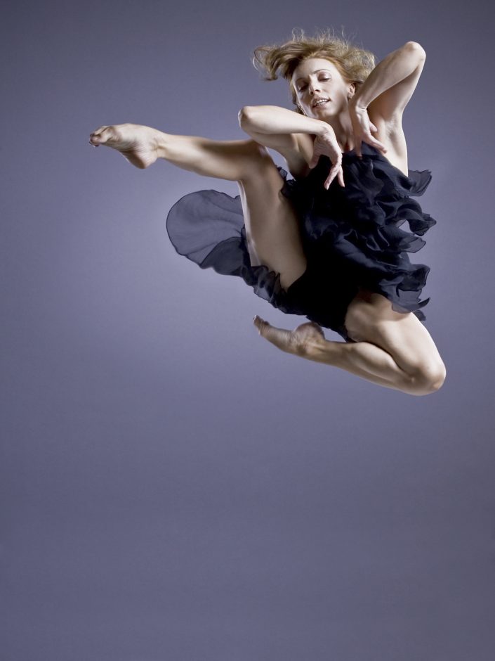 Jerry Metellus dance photography at JM Studios Las Vegas. Contemporary photography of female ballet dancer Jete captured in mid-air with elbows extended in a black dress.