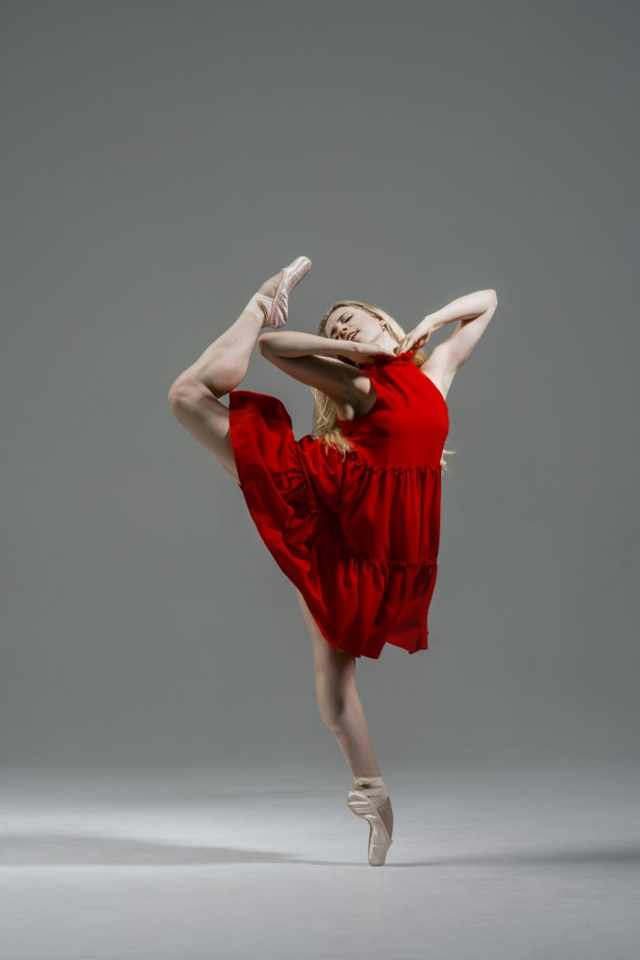 Jerry Metellus dance photography at JM Studios Las Vegas. Ballet photography of a dancer in a red dress doing a difficult ballet dance on the toes of her left foot.