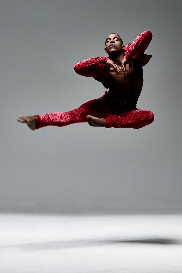 Jerry Metellus dance photography at JM Studios Las Vegas. Ballet photography of a dancer dressed in a red suit jumping with his elbows flared.