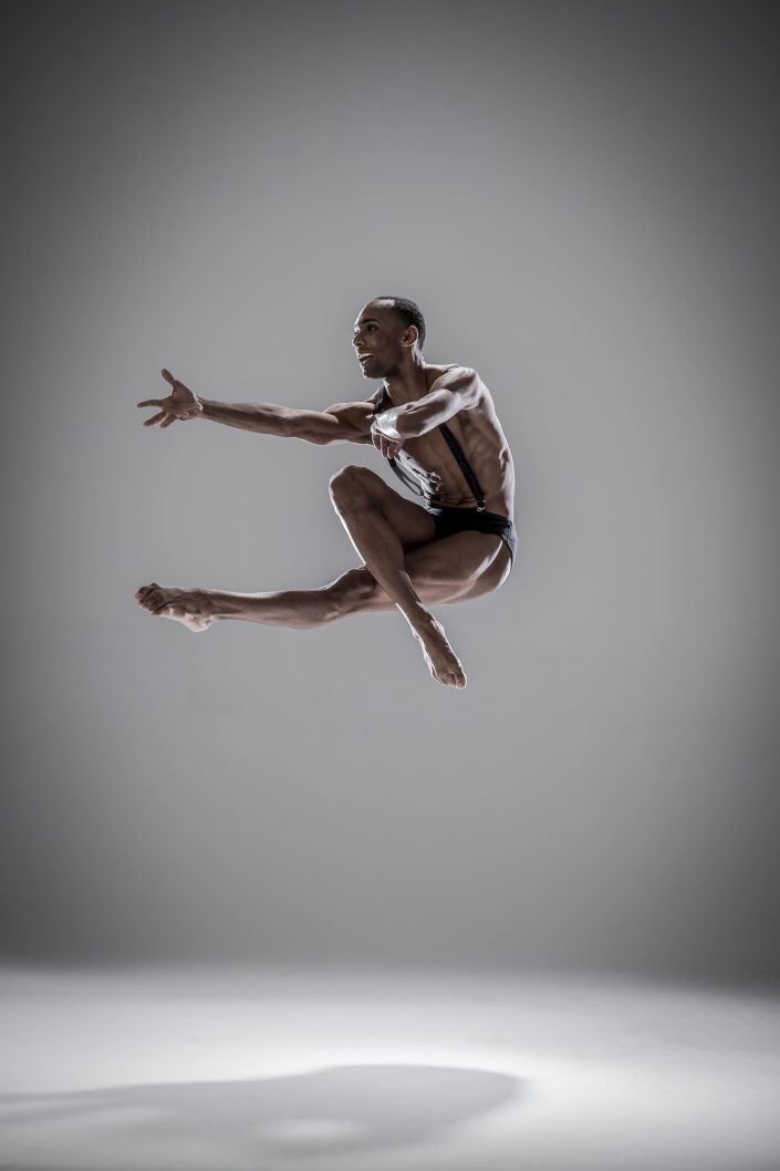 Jerry Metellus dance photography at JM Studios Las Vegas. Contemporary photography of a dancer in black suspenders leaping with one hand outstretched.
